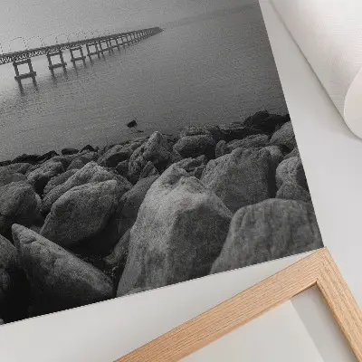 Nowoczesna grafika na płótnie spokojny pejzaż z mostem na kamienistej plaży przy szarym niebie