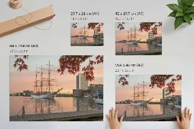 Plakat do salonu żaglowiec o zachodzie słońca na tle spokojnej panoramy miasta